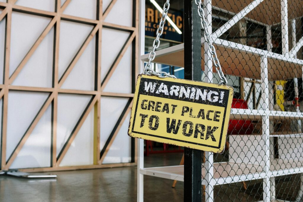 Żółta tabliczka z napisem „WARNING! GREAT PLACE TO WORK” w nowoczesnym biurze.