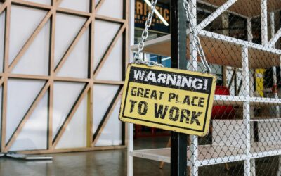 Żółta tabliczka z napisem „WARNING! GREAT PLACE TO WORK” w nowoczesnym biurze.